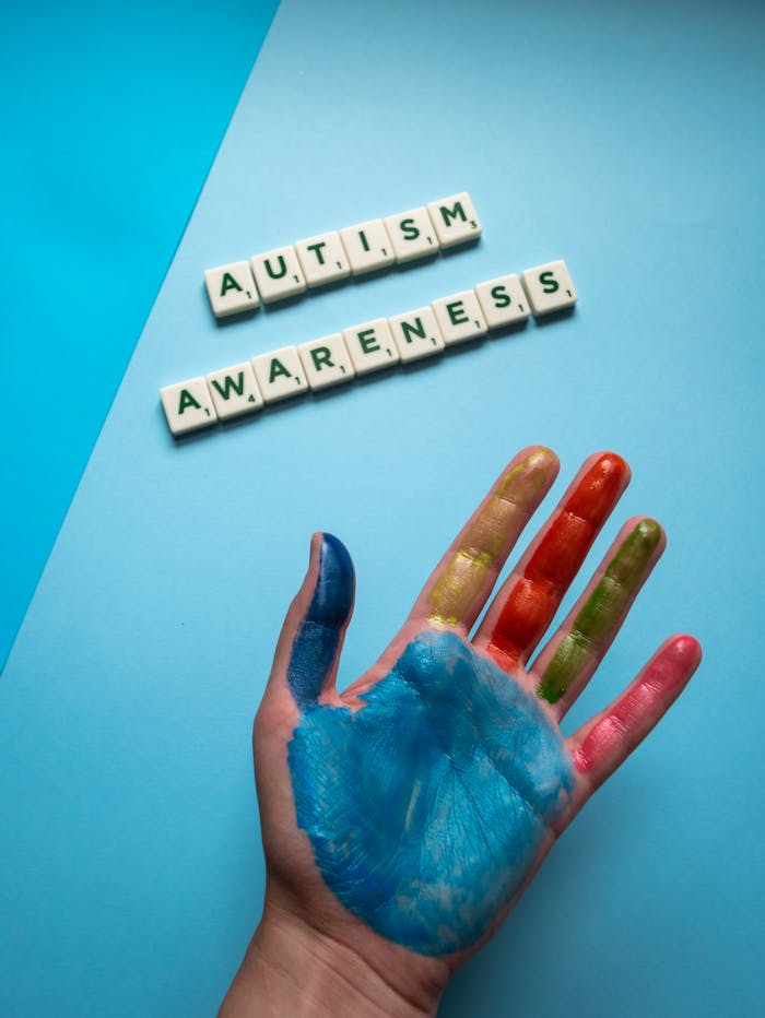 services-01 A top view of a colorful painted hand next to autism awareness scrabble tiles on a blue background.