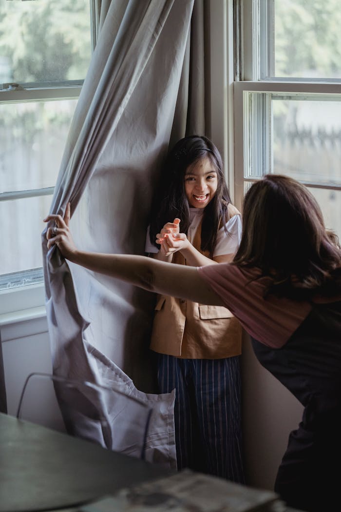 missions A mother and daughter enjoy a playful moment playing hide and seek by the window indoors.