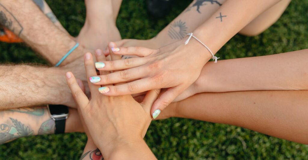 A group of people's hands with tattoos and colorful nails symbolizing unity on grass.